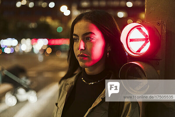 Woman by red traffic arrow sign at night
