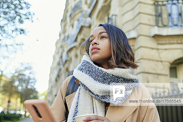 Thoughtful woman with scarf and mobile phone in city