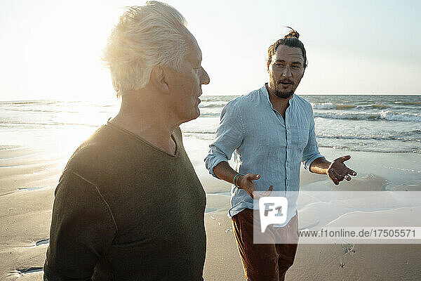 Sohn gestikuliert im Gespräch mit Vater am Strand