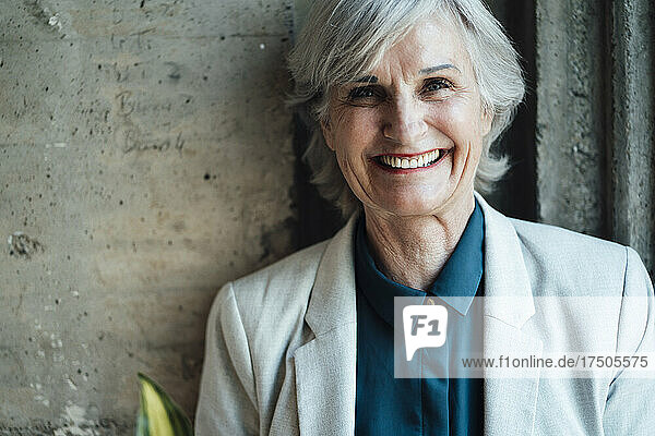 Smiling senior businesswoman in front of wall