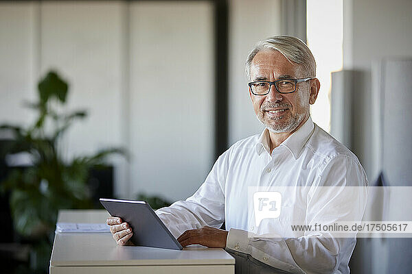 Smiling businessman with tablet computer at counter in office