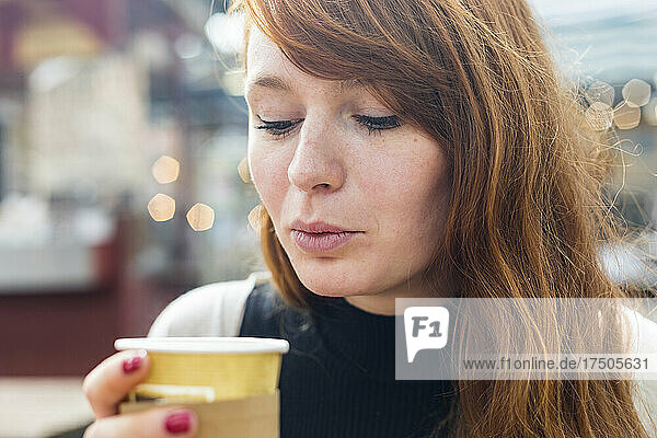 Woman blowing coffee in disposable cup at cafe
