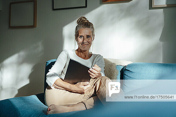 Smiling woman holding tablet PC on sofa in living room