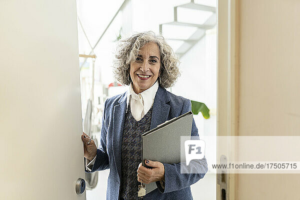 Smiling real estate agent with file standing on doorway at apartment