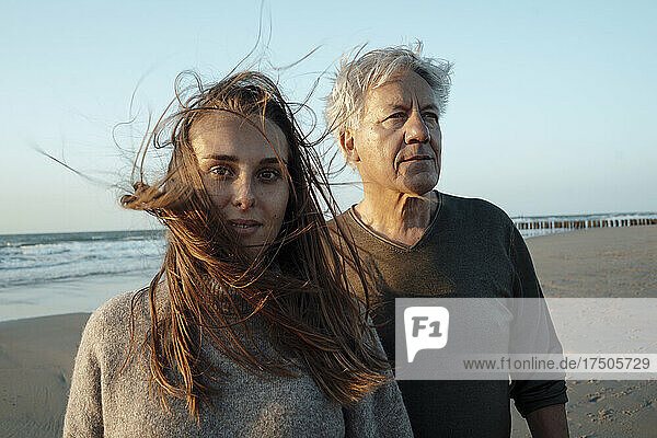Daughter with windswept hair standing with father at beach
