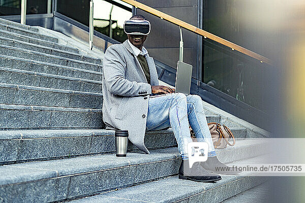 Geschäftsmann mit Virtual-Reality-Headset und Laptop sitzt auf Stufen