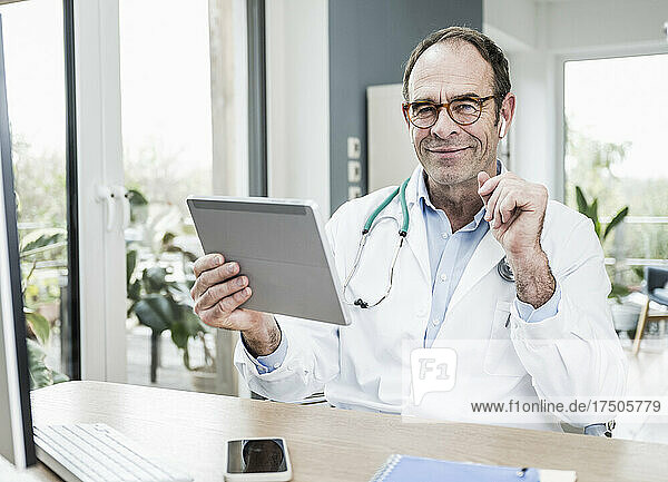 Smiling doctor with tablet PC at desk in hospital