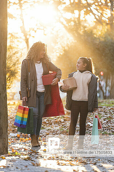 Lächelnde Mutter und Tochter mit Einkaufstüten und Weihnachtsgeschenken stehen auf dem Fußweg