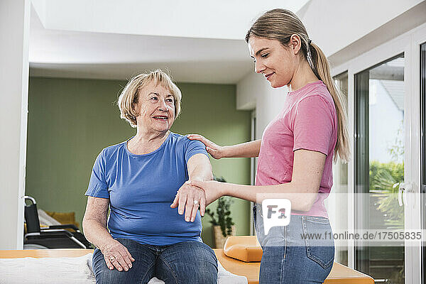 Young physiotherapist helping patient to stretch hand at home