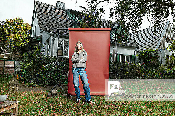 Frau mit verschränkten Armen vor rotem Hintergrund im Hinterhof
