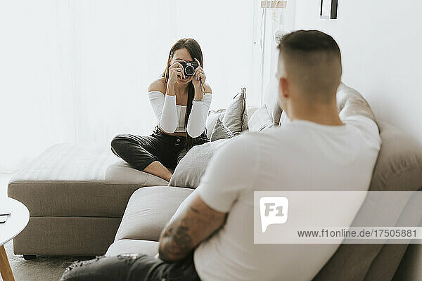 Woman photographing man through camera in living room