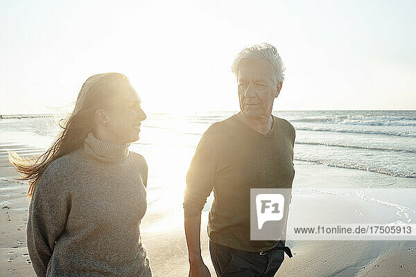 Smiling woman with father walking at beach on sunny day