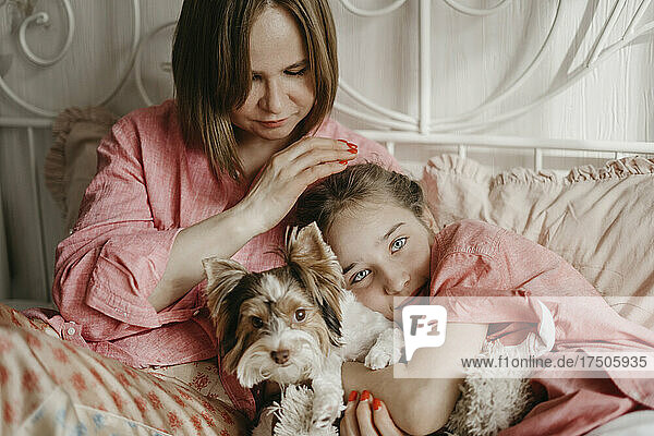Mother and daughter relaxing with dog on bed at home