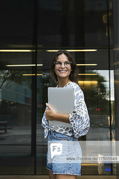 Smiling young businesswoman with laptop looking away