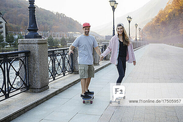 Paar hält sich an den Händen und fährt gemeinsam Skateboard auf Fußweg