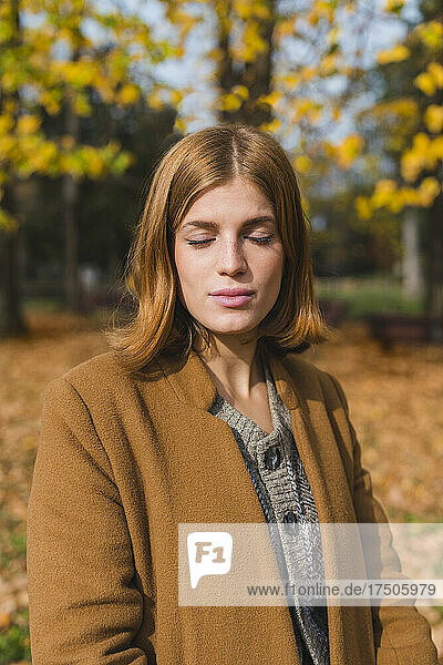 Young woman with eyes closed standing in autumn park