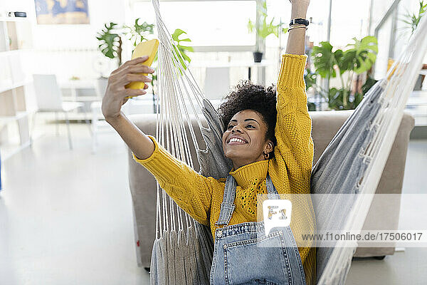 Smiling young woman filming through smart phone on swing at home