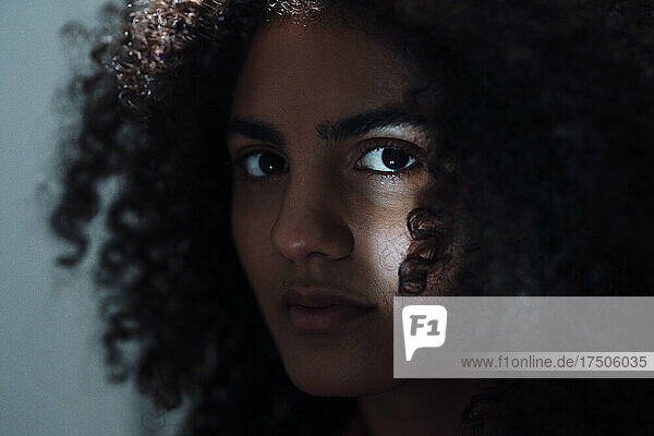 Serious young woman with curly hair in dark