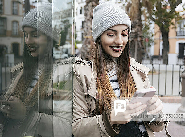 Woman using smart phone leaning on glass wall