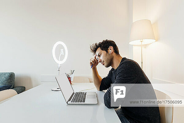 Young businessman with pen working on laptop at home office