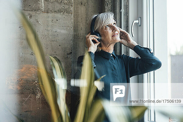 Businesswoman with wireless headphones looking out of window