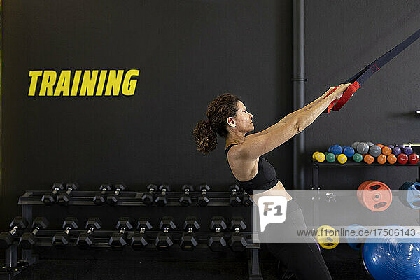 Sportswoman pulling straps by dumbbells in gym