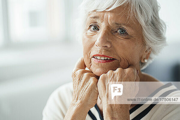Senior woman with hands on chin at home