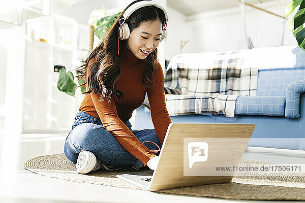 Businesswoman with headphones using laptop on carpet