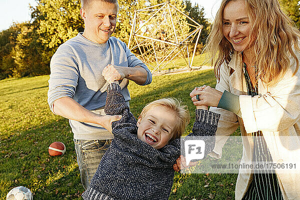 Happy parent swinging cute son at park