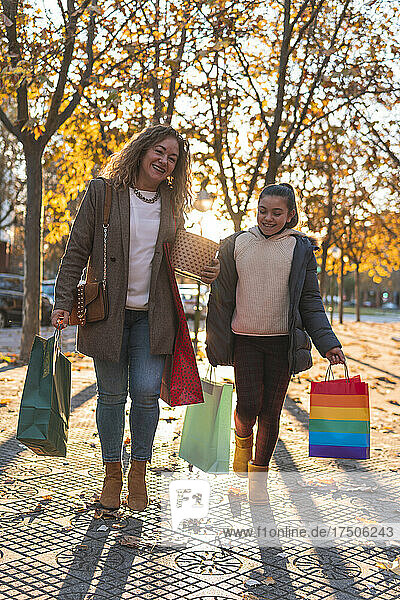 Lächelnde Mutter und Tochter mit Einkaufstüten gehen auf Fußweg