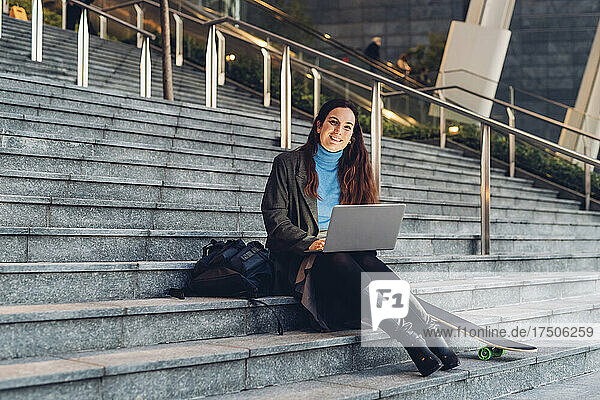 Lächelnde Geschäftsfrau mit Laptop sitzt auf Stufen