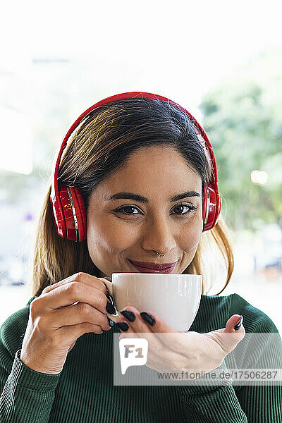 Smiling woman with wireless headphones and coffee cup at cafe
