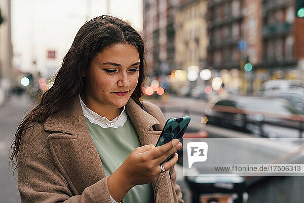 Young woman in overcoat using mobile phone