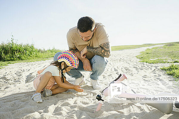 Father looking at daughter playing with sand on sunny day