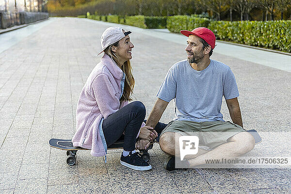 Paar redet miteinander und sitzt auf dem Skateboard am Fußweg