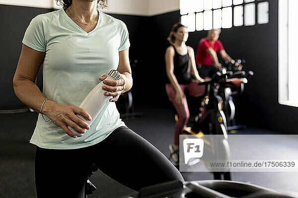 Sportswoman holding water bottle on exercise bike at gym