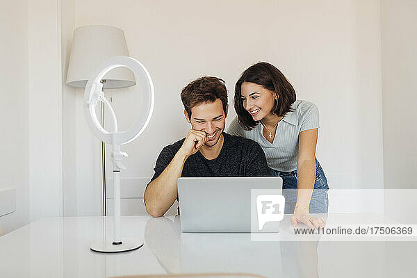 Happy young woman looking at male freelancer working on laptop at home