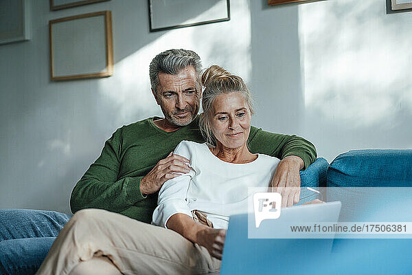 Paar sitzt mit Laptop zu Hause gemeinsam auf dem Sofa
