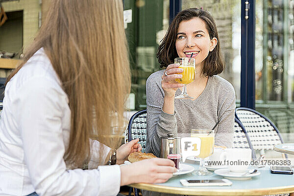 Smiling woman drinking juice by friend in cafe