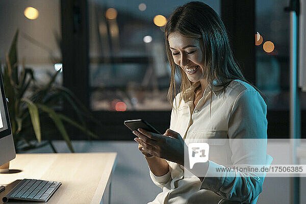 Smiling businesswoman using mobile phone in office at night