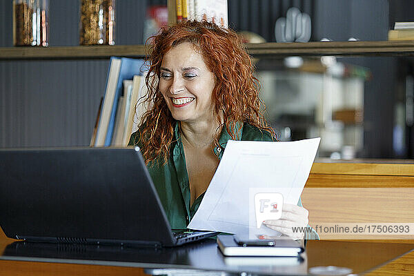 Businesswoman with document using laptop at cafe table