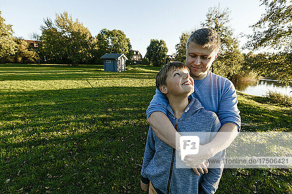 Smiling boy looking at father embracing in park