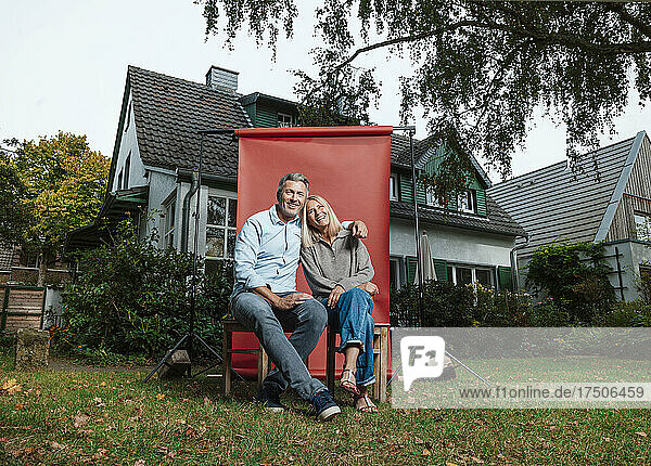 Smiling couple sitting on stools in front of backdrop