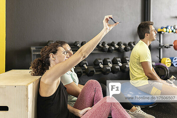 Athlete with friend taking selfie through smart phone in gym