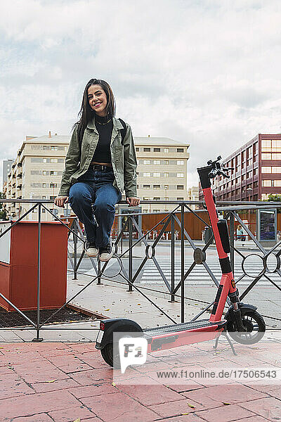Frau mit Elektroroller sitzt auf Geländer