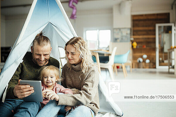 Happy family sitting inside tent using digital tablet at home
