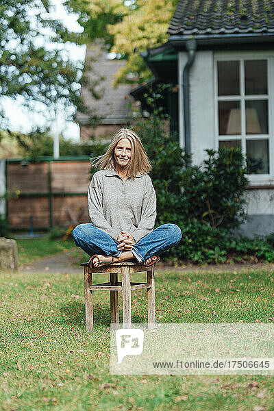 Smiling woman sitting cross-legged on stool at backyard