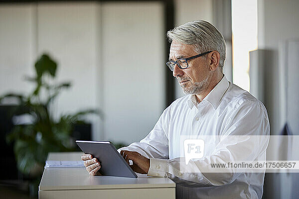 Mature businessman working on tablet PC at counter in office