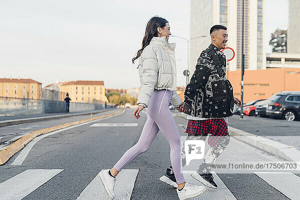 Young couple holding hands and crossing street in city