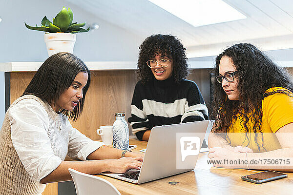Young businesswomen looking at colleague discussing in coworking office